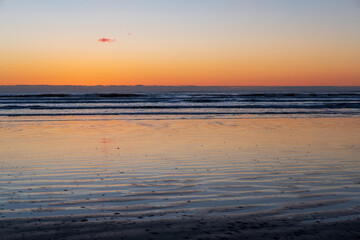 A beach with reflective sand at sunset, clouds streaking across the sky