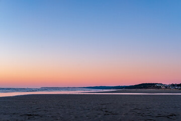 A beach with reflective sand at sunset, clouds streaking across the sky