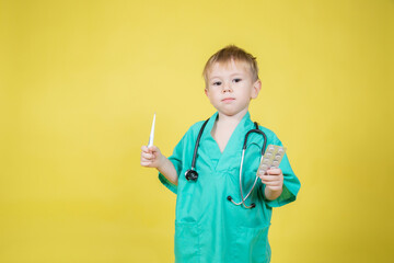 Portrait of little caucasian boy dressed in doctors coat holds pills