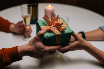 Close-up high-angle view of woman giving box with gift to man sitting at table with candles on...