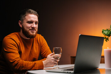 Close-up of happy young man enjoying distant dating using laptop computer, holding glass with champagne, talking celebration toasting via video call. Couple in love chatting on remote date.
