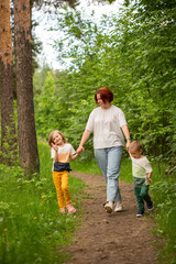 Fototapeta premium Mom walks with two children in the summer in the forest