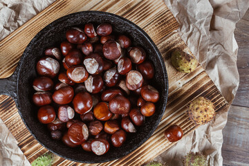 Close up view of chestnuts in a cast iron pan on a wooden background