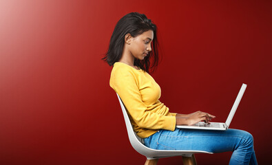 Deep in the world wide web. Studio shot of an attractive young woman using a laptop against a red background.