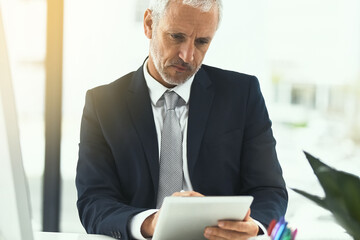 He takes technology seriously in his work. Shot of a mature businessman using a digital tablet while sitting at his desk in an office.