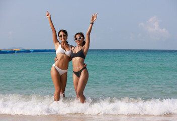 Couple Tanned women wearing bikini hand to hand walk to the sea, LGBT and summer vacation concept , Portrait sexy tanned woman hug and hand up on tropical beach