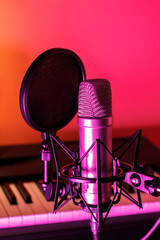 Close up of microphone with pop filter in front of piano keys with purple, pink, and orange ambient lighting.