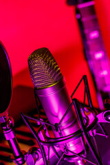 Closeup of microphone in neon purple lighting with electronic instruments in background.