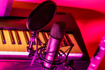 Close up of microphone with pop screen in front of electronic piano keys in vibrant neon lighting. 