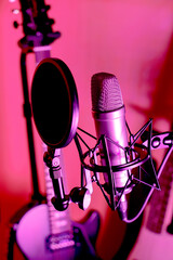 Closeup of microphone with pop screen and electronic guitar in background in purple lighting. 