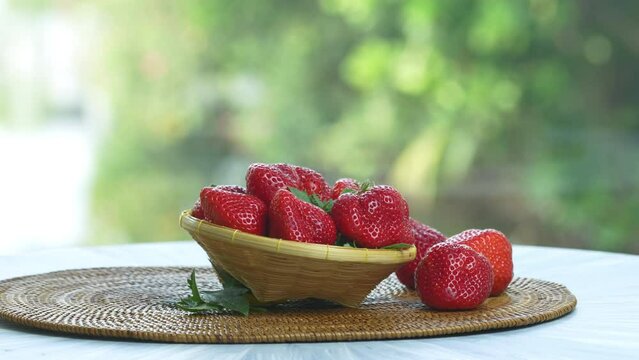 Red strawberry in Bamboo basket on wooden table, Fresh Red strawberries with leaves over green natural Blur background.
