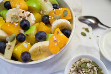 The concept of low-calorie delicious desserts. A bowl of fruit salad. Natural unprocessed organic food. A delicious sweet snack on a light background. Green apple, banana, pineapple, grapes, peaches