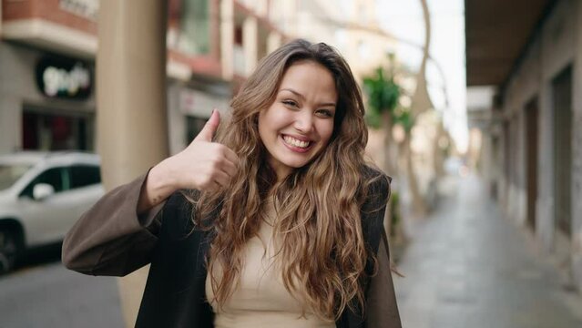 Young hispanic woman smiling confident doing ok sign with thumb up at street