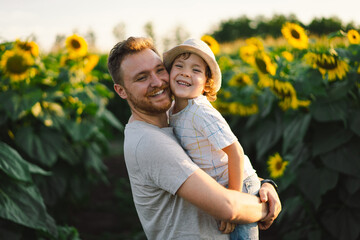 Father with little baby son in sunflowers field during golden hour. Dad and son are active in...