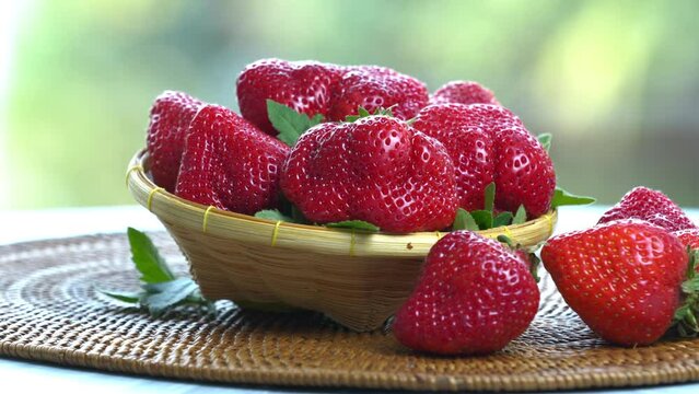 Red strawberry in Bamboo basket on wooden table, Fresh Red strawberries with leaves over green natural Blur background.