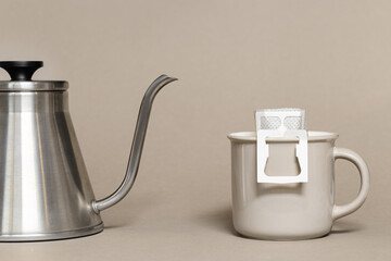 Drip coffee bag with ground coffee in big cup, hot water is poured into paper filter drip coffee for brewing on beige color background, quick way to brew ground coffee