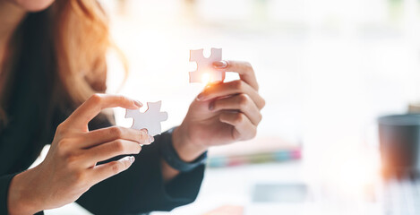 Cropped shot of Businesswoman hand connecting jigsaw puzzle with sunlight effect, Business solutions, success and strategy concept.