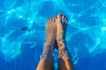 Barefoot of a slender Latin woman, under the clear surface of the water in a swimming pool.