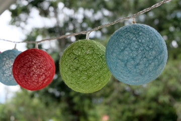 Cool colourful blue, green and red round textured bubble bauble lights hanging outdoors during a celebration with trees in background