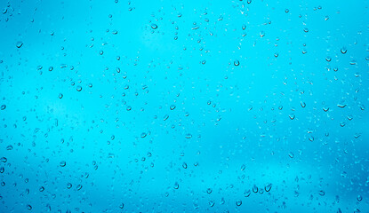 Rain drops, water drops of rain on a window glass blue background, abstract defocused with space