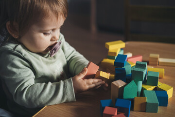 Baby girl with a pacifier in his mouth is playing with the colorful figurines on his table. Children education. Healthy lifestyle. Baby development.