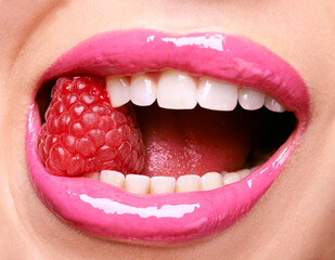 Ravishing raspberries. Shot of a woman wearing pink lipstick and biting into a raspberry.