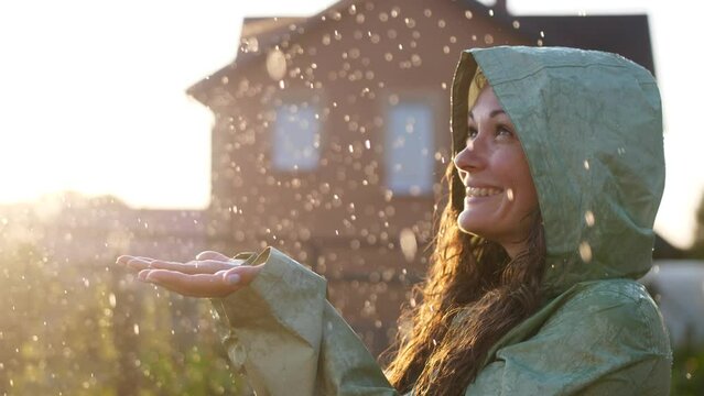 Young happy woman wearing raincoat is feeling free and smiling under the rain. Concept of life, freedom, nature, adventure, purity.