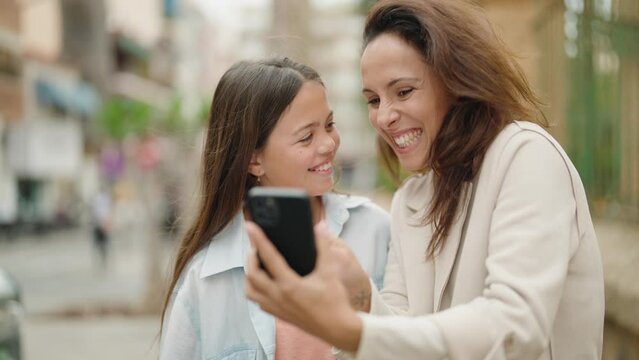 Mother and daughter using smartphone standing together at street