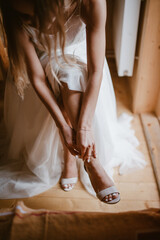 Fototapeta na wymiar Close-up portrait of bride's hands putting on elegant beige shoes sitting on chair idoor. Wedding preparation.