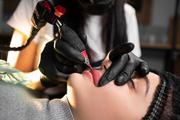 master of permanent makeup in a beauty salon applies a tattoo on the client's lips.