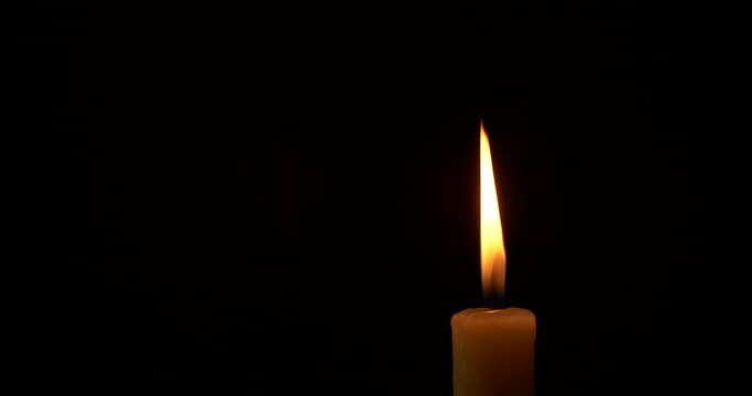 Closeup burning single candle flame isolated on black background
