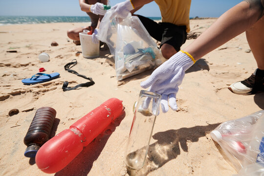 Close-up image of volunteers picking up glass and plastic trash on sea beach
