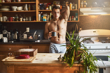 Enjoying a cup of coffee in the kitchen. Cropped shot of a handsome young shirtless man drinking a cup of coffee in the kitchen at home.