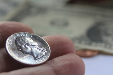 Man's hand picking up a quarter coin from a pile of banknotes and coins.