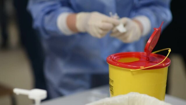 Doctor throws a used syringe and medical waste into a plastic container