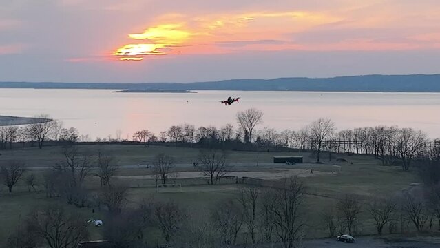 An aerial view over Calvert Vaux Park in Brooklyn, NY during a cloudy evening. The drone camera pan left, following an FPV drone hovering with Gravesend Bay in the background.