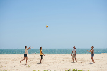 Group of happy young people ing volleyball on beach on sunny day