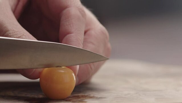 Slow motion man cut physalis in halves on wood board
