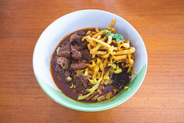 Above view of Khao Soi Thai style. Northern Thai Curry Noodles with Beef on wooden table at the restaurant. Recipe popular traditional Thai Asian style Lanna food. Top-down
