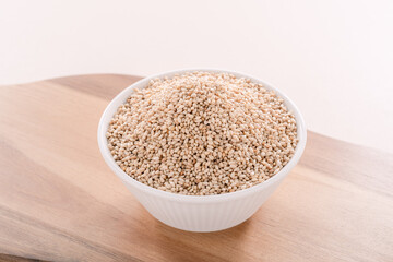 Sesame seeds in a white bowl on a wooden plate.