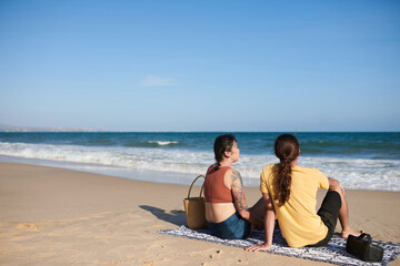 Young couple relaxing on beach, sitting on blanket and enjoying sea view