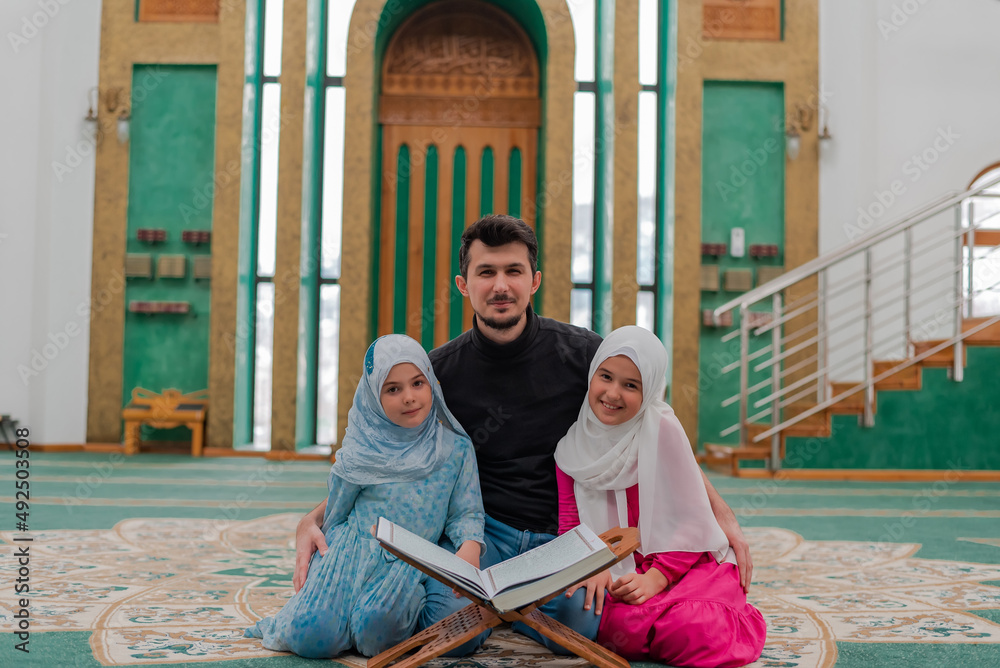 Wall mural happy muslim family reading a holy book quran in the mosque. father teaching child daughter islam re