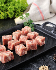 Raw Saikoro Cubes Beef Steak on Steak Plate with Lettuce at Background, Above Black Table.