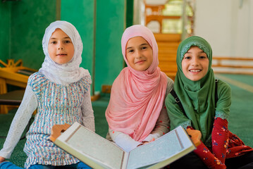 Group of a children reading a holy book Quran in the mosque. Happy Muslim family. Muslim girls in...