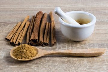 Cinnamon powder on a wooden spoon with mortar and cinnamon sticks