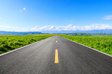 Straight asphalt road and green grass with mountain scenery under blue sky