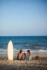 Family of three sitting on blanket on beach and looking at sea waves