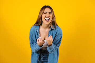 young latin woman gesturing YES, celebrating success or achievement, feeling excited on yellow...