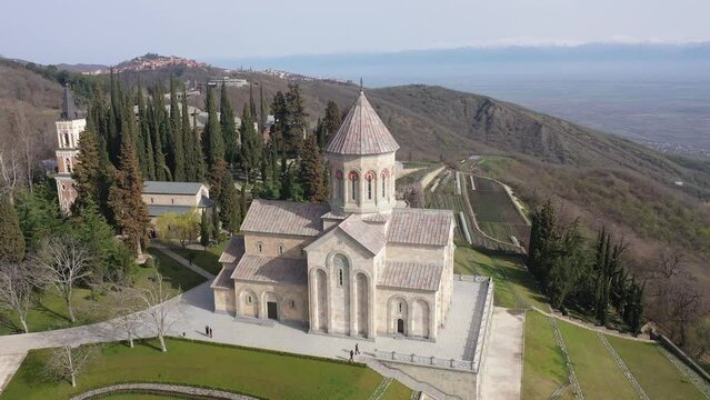 Scenic spring aerial view of Church of St. Nino in monastic complex of Bodbe nunnery on hillside overlooking Alazani Valley and Greater Caucasus mountains in background, Sighnaghi, Kakheti, Georgia