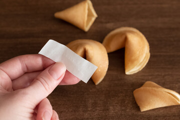 Person holds in hand blank paper slip from fortune cookie against few cookies laying on table...